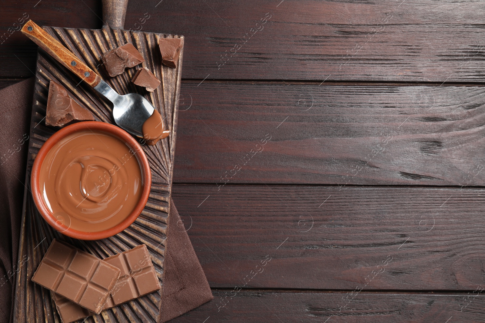 Photo of Tasty milk chocolate paste in bowl and pieces on wooden table, top view. Space for text