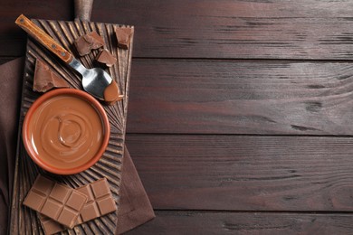 Photo of Tasty milk chocolate paste in bowl and pieces on wooden table, top view. Space for text