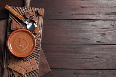 Tasty milk chocolate paste in bowl and pieces on wooden table, top view. Space for text