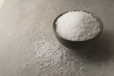 Photo of Natural salt in bowl on grey table, space for text