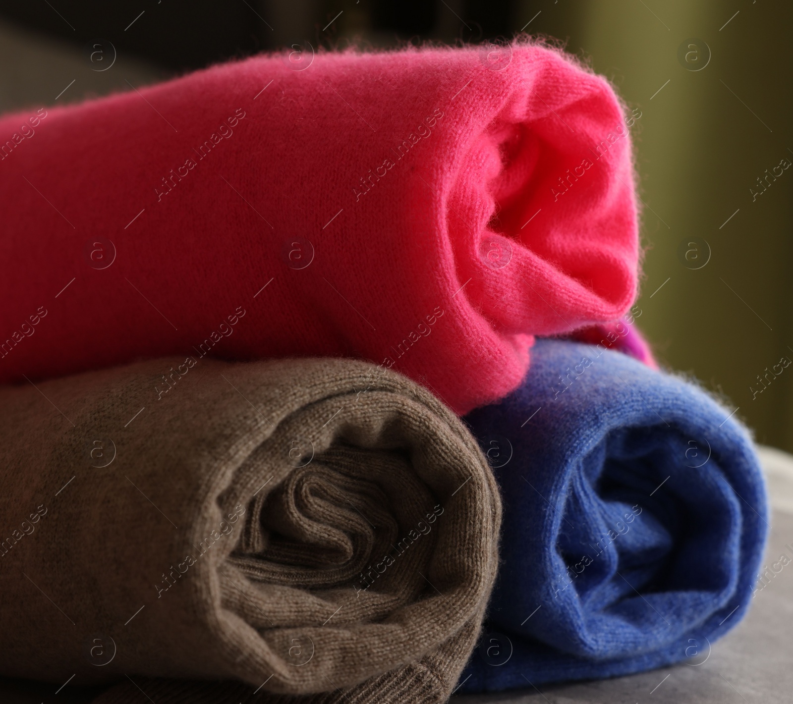 Photo of Rolled color sweaters on gray table, closeup. Space for text