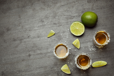 Photo of Mexican Tequila shots, lime slices and salt on grey table, flat lay. Space for text