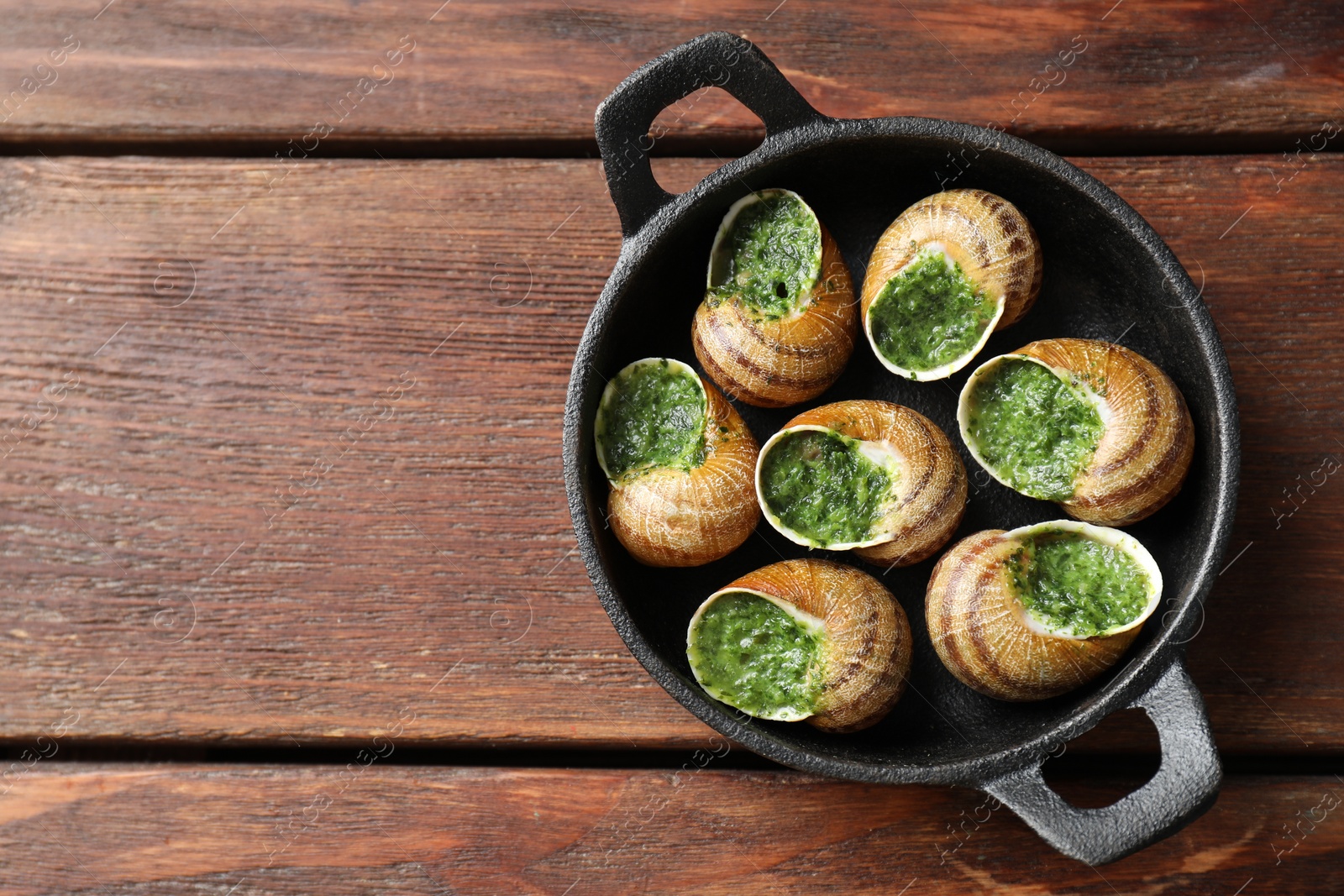 Photo of Delicious cooked snails in baking dish on wooden table, top view. Space for text