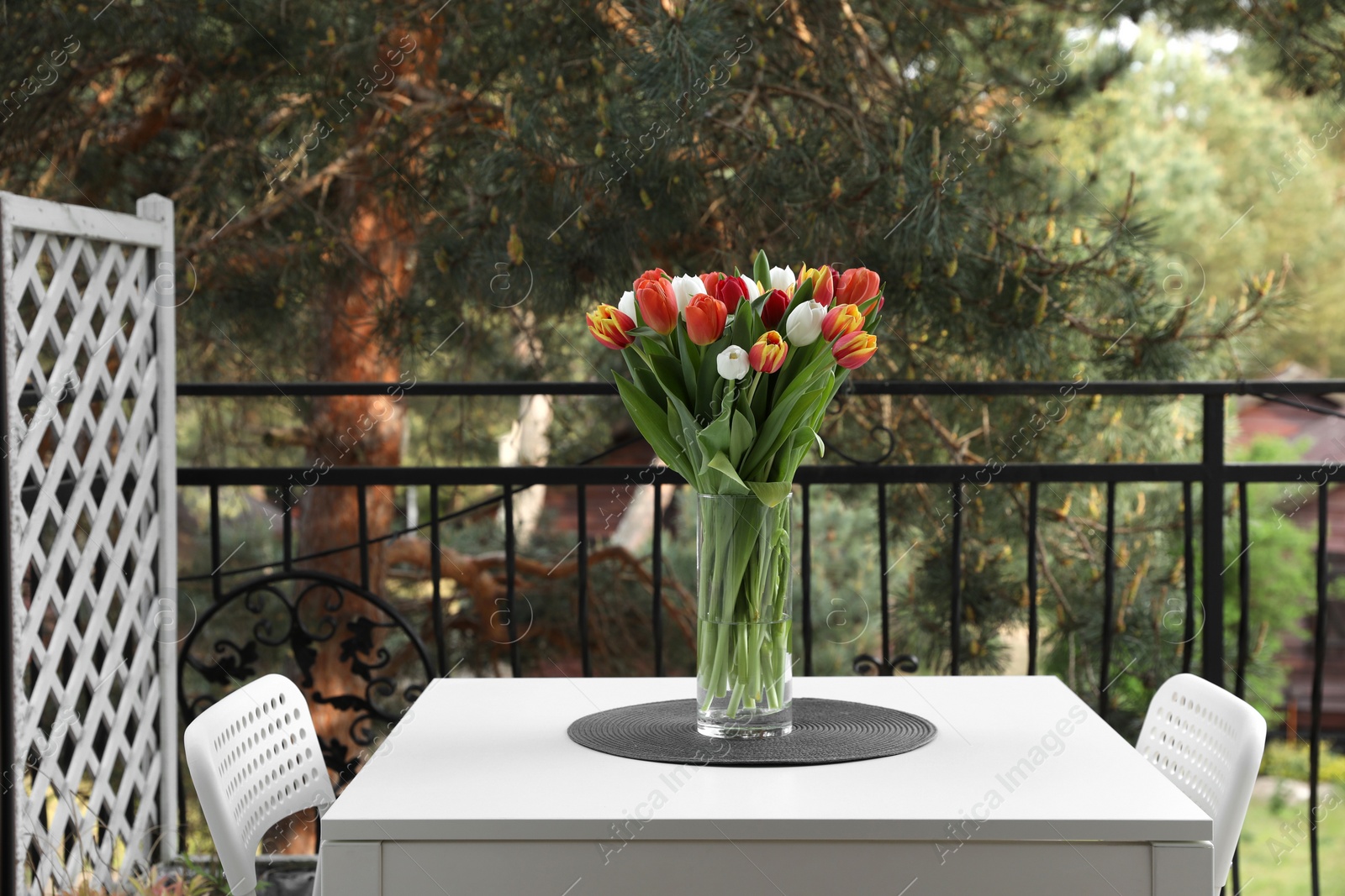 Photo of Beautiful colorful tulips in glass vase on white table at balcony