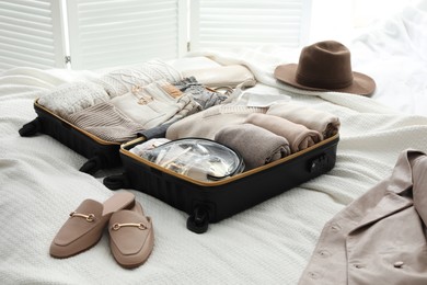 Open suitcase with folded clothes, shoes and accessories on bed