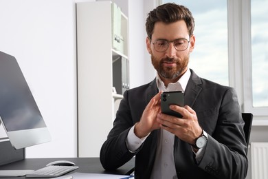 Handsome businessman using smartphone at workplace in office, space for text