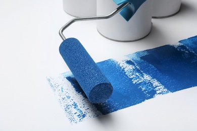 Photo of Roller brush with blue paint near cans on white background