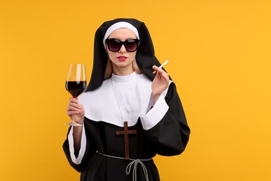 Photo of Woman in nun habit holding glass of wine and cigarette against orange background