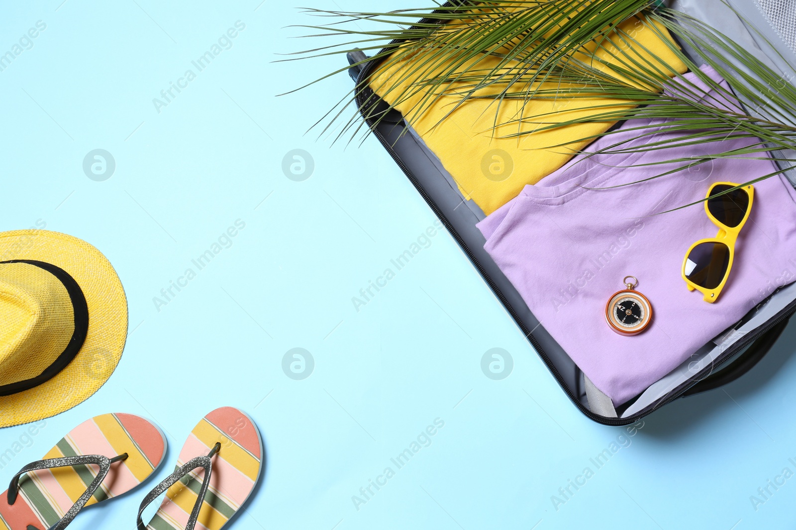 Photo of Suitcase and beach accessories on light blue background, flat lay. Space for text