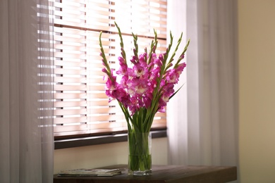 Photo of Vase with beautiful pink gladiolus flowers on wooden table in room, space for text