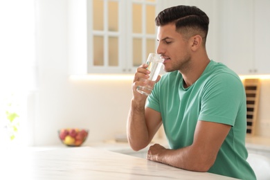 Man drinking pure water from glass at table in kitchen. Space for text