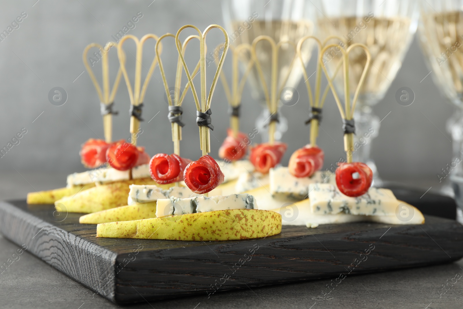 Photo of Tasty canapes with pears, blue cheese and prosciutto on grey table, closeup