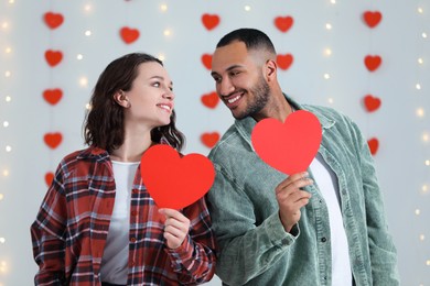 Photo of Lovely couple with red paper hearts indoors. Valentine's day celebration