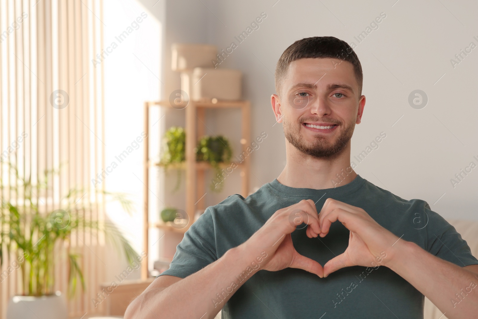 Photo of Happy volunteer making heart with his hands in room. Space for text