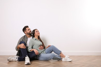 Photo of Young couple sitting on floor near white wall indoors. Space for text