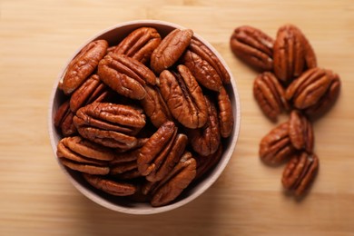 Photo of Tasty pecan nuts with bowl on wooden table, flat lay