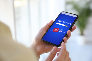 Woman holding smartphone with online shopping website on screen indoors, closeup