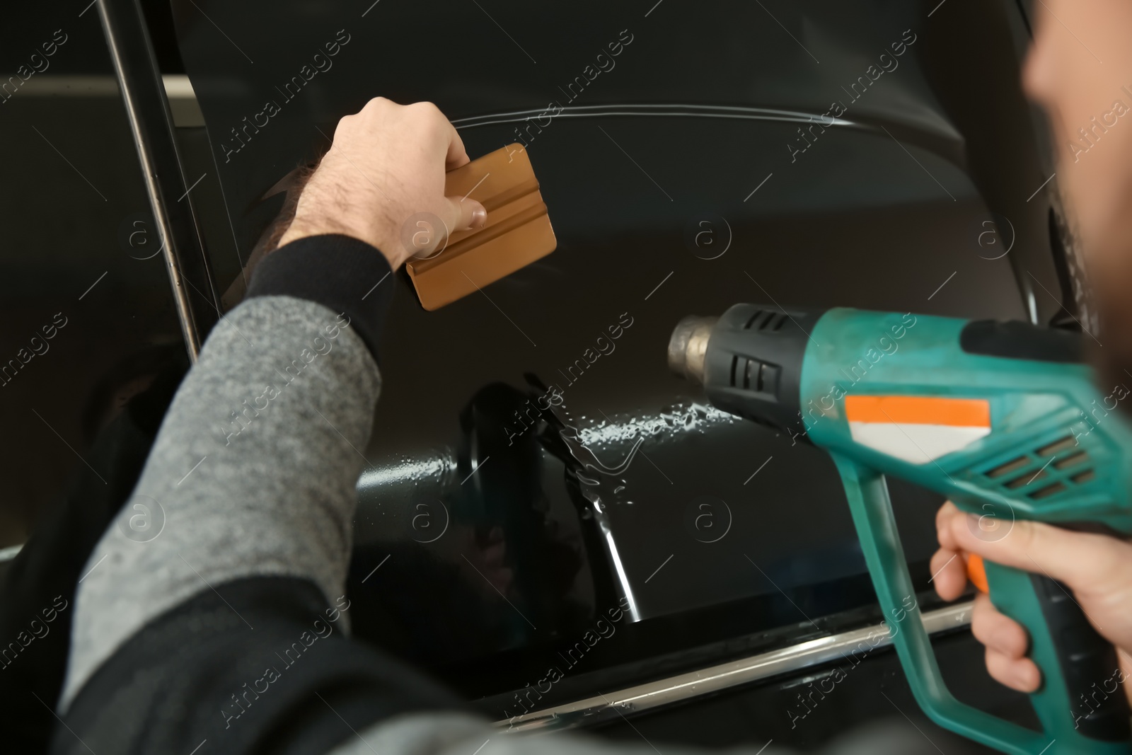 Photo of Worker tinting car window in shop, closeup