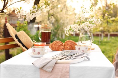 Stylish table setting with tea and croissants in spring garden