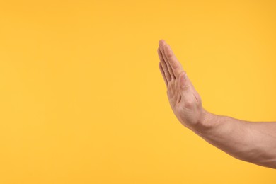Photo of Man showing stop gesture on orange background, closeup and space for text