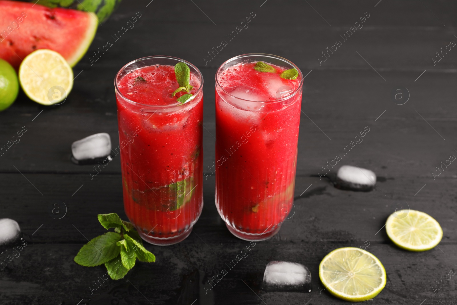 Photo of Glasses of delicious fresh watermelon juice, lime, mint and ice on black wooden table