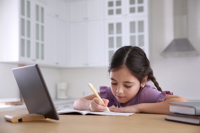 Photo of Little girl doing homework with modern tablet at home