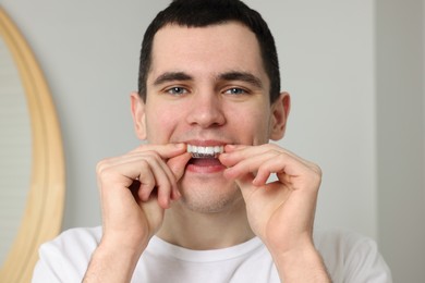Young man applying whitening strip on his teeth indoors
