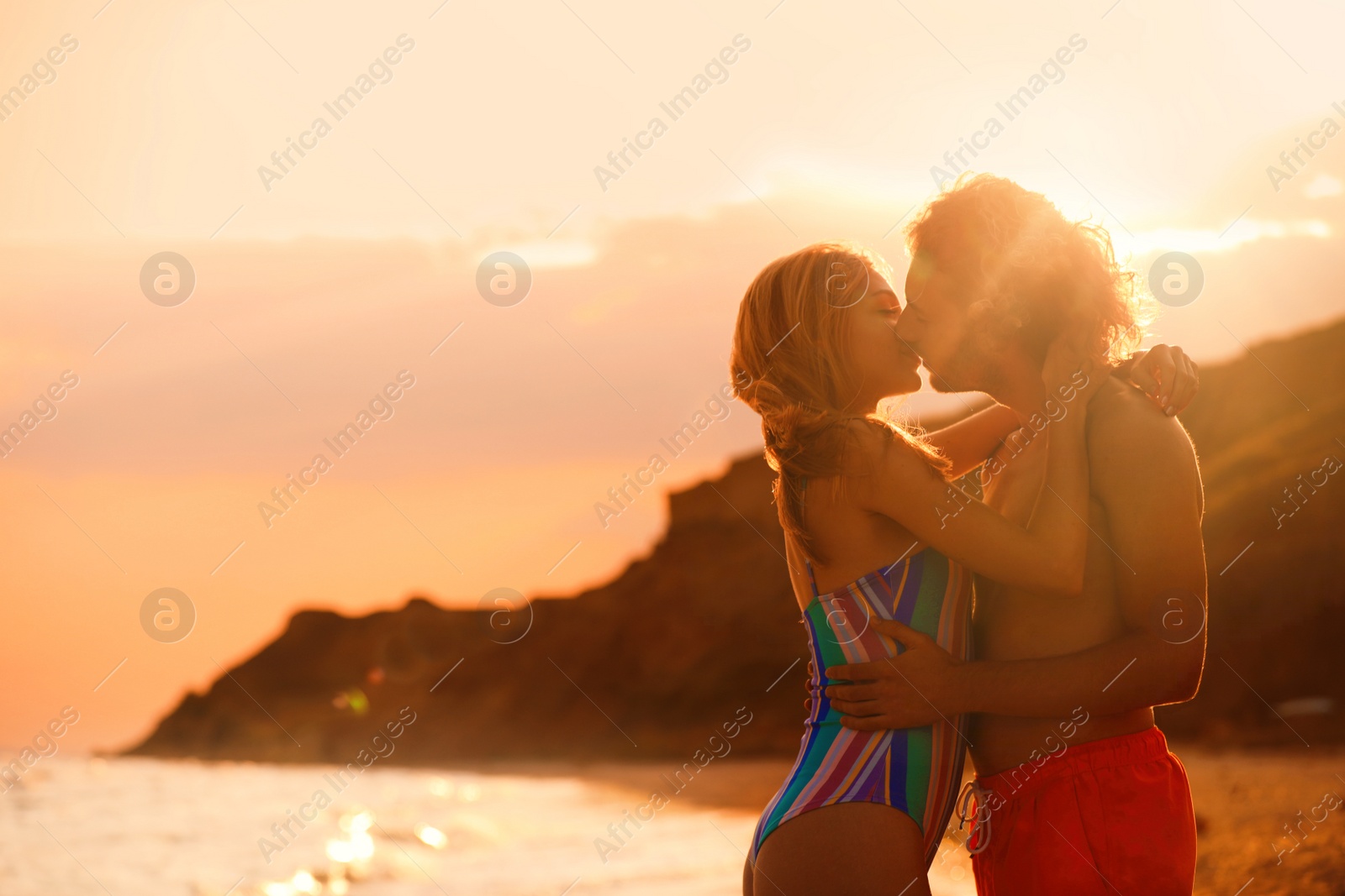 Photo of Young woman in bikini kissing her boyfriend on beach at sunset. Lovely couple