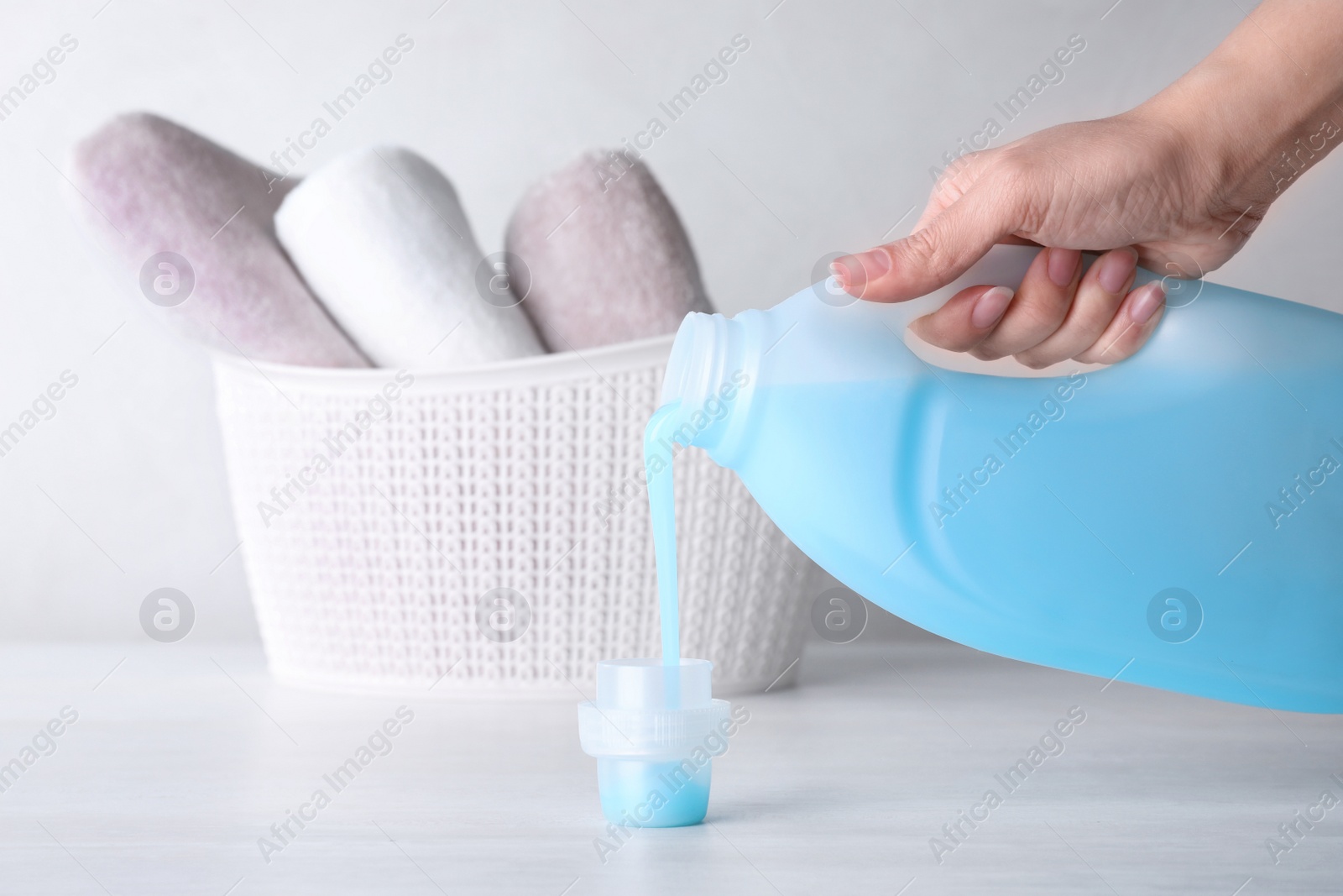 Photo of Woman pouring laundry detergent into cap on table against light background, closeup