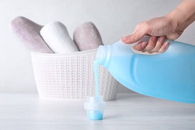 Woman pouring laundry detergent into cap on table against light background, closeup