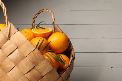 Photo of Wicker basket with whole and cut ripe oranges on wooden background, closeup. Space for text