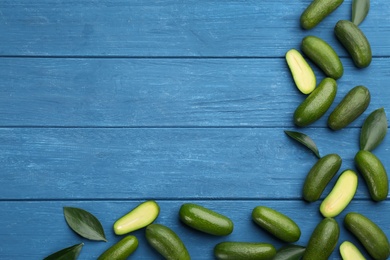 Fresh seedless avocados with green leaves on blue wooden table, flat lay. Space for text