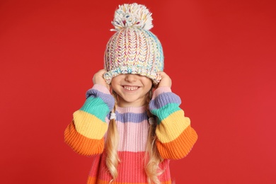 Photo of Cute little girl in hat and warm sweater on red background. Winter season