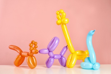 Animal figures made of modelling balloons on table against color background