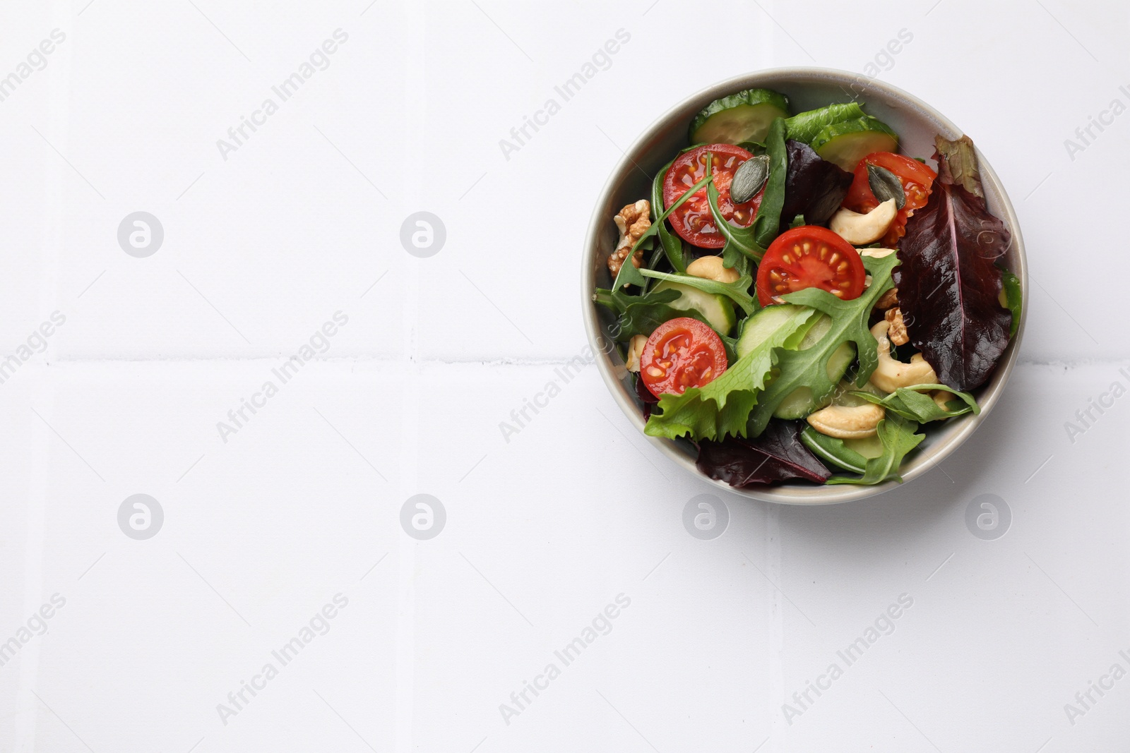 Photo of Tasty fresh vegetarian salad on white tiled table, top view. Space for text