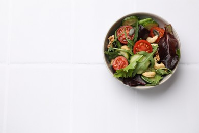 Tasty fresh vegetarian salad on white tiled table, top view. Space for text