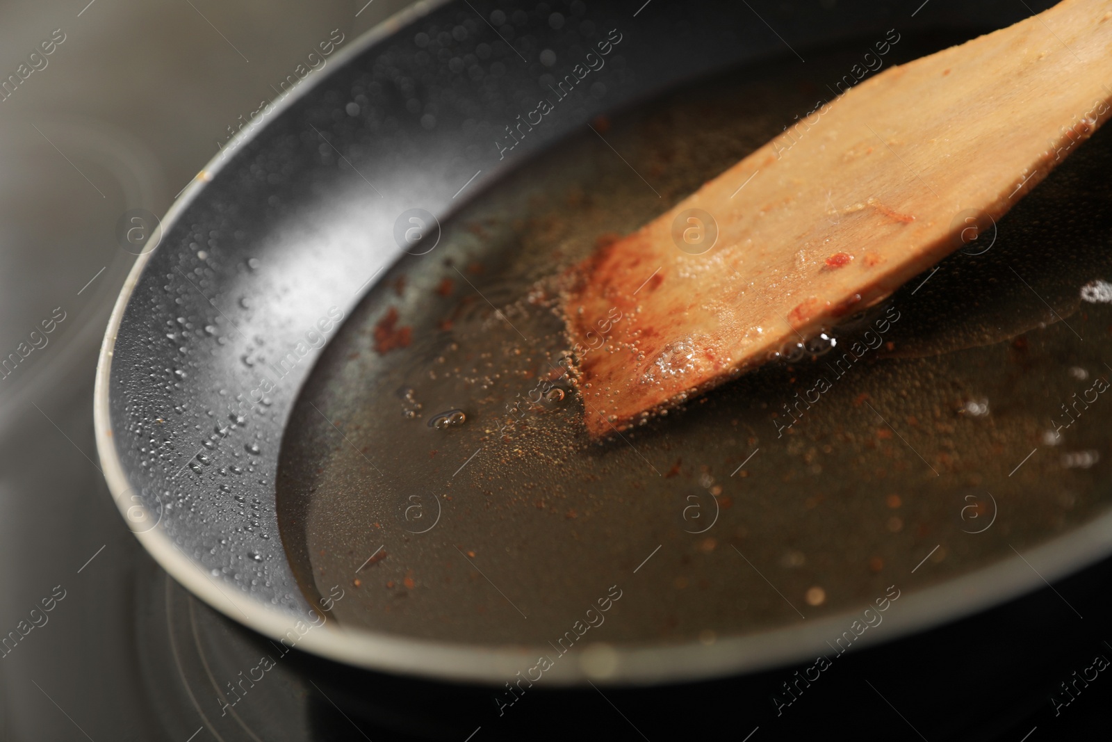 Photo of Frying pan with spatula and used cooking oil on stove, closeup