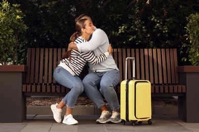 Long-distance relationship. Beautiful couple hugging on bench and suitcase outdoors