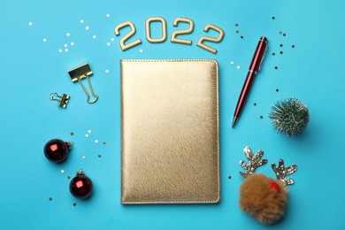 Golden planner and Christmas decor on light blue background, flat lay. Planning for 2022 New Year