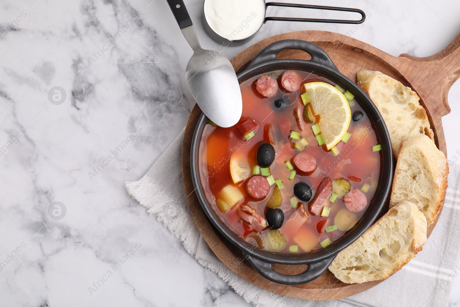 Photo of Meat solyanka soup with thin dry smoked sausages served on white marble table, flat lay. Space for text