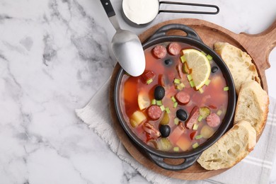 Meat solyanka soup with thin dry smoked sausages served on white marble table, flat lay. Space for text