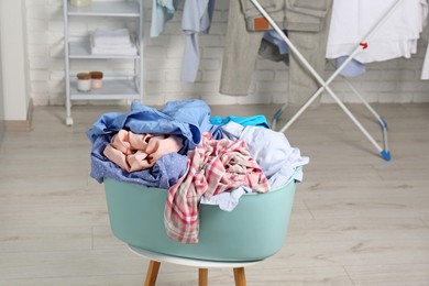 Photo of Plastic laundry basket overfilled with clothes on white stool indoors