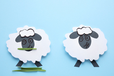 Paper sheeps on light blue background, flat lay. Concept of jealousy