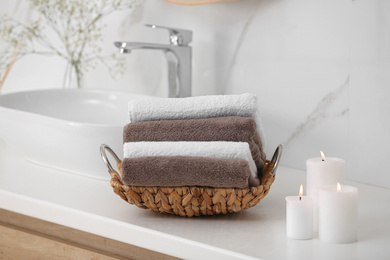 Photo of Basket with clean towels and burning candles on counter in bathroom
