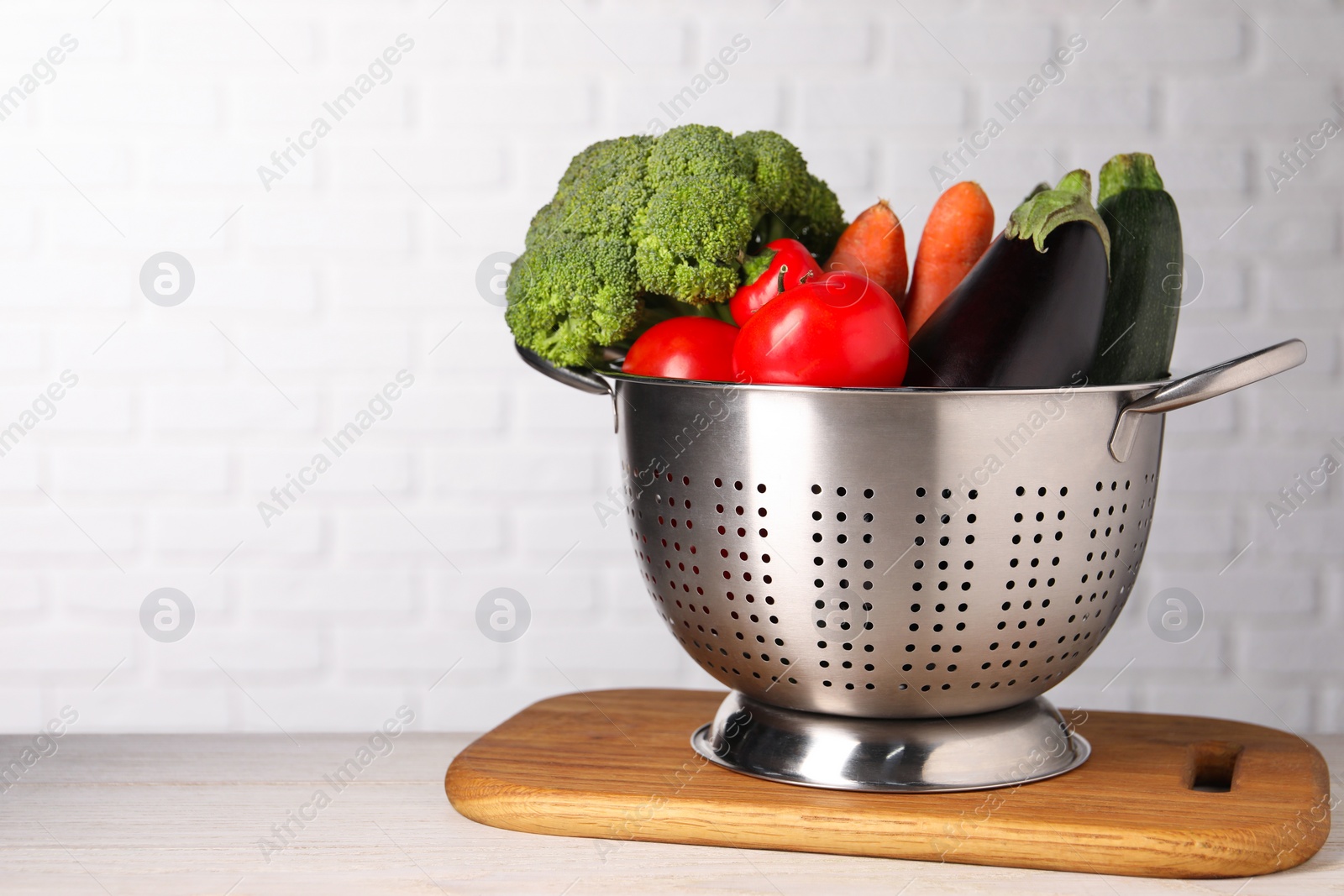 Photo of Fresh vegetables in colander on white wooden table. Space for text