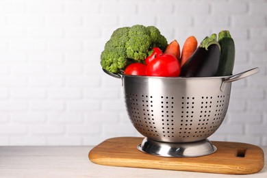 Fresh vegetables in colander on white wooden table. Space for text