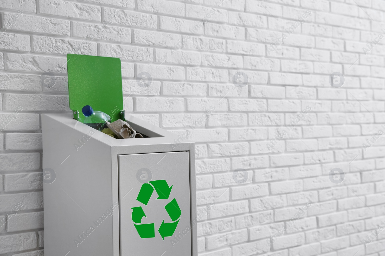 Photo of Overfilled trash bin with recycling symbol near brick wall. Space for text