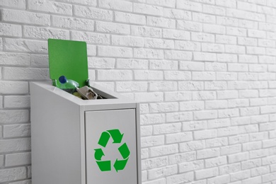 Overfilled trash bin with recycling symbol near brick wall. Space for text