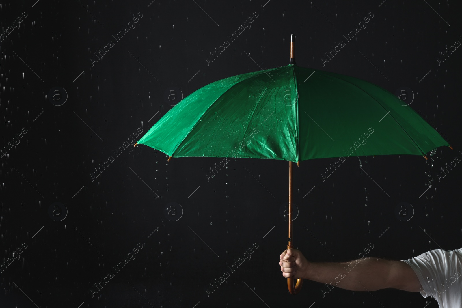 Photo of Man holding green umbrella under rain against black background, closeup