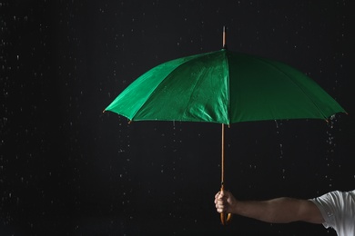 Photo of Man holding green umbrella under rain against black background, closeup